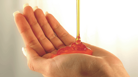 En genomskinlig, gyllene vätska hälls i en hand, möjligtvis schampo eller hårolja.