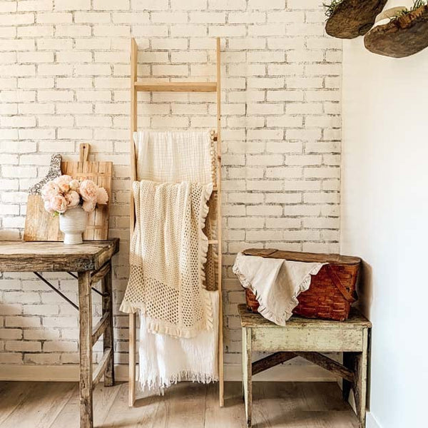 A table, wooden ladder, and basket on top of a low stool with a faux brick wall in the background