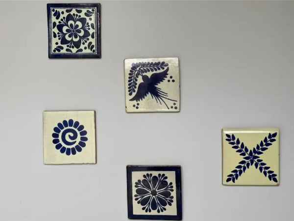 Square ceramic tiles displayed on a wall. The tiles have various painted designs