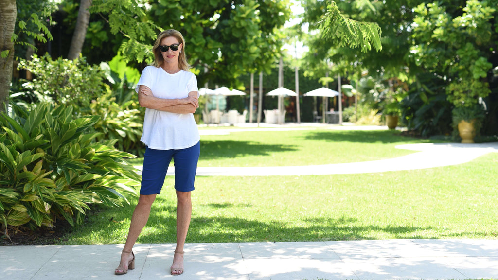 Val standing in a white tee and navy bermuda shorts