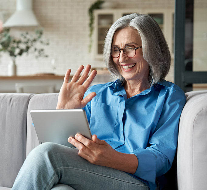 A senior middle aged woman sitting on the sofa and having a video call and receiving support and care reemotely from an Auzen audiologist. 