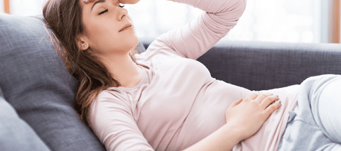 Woman on couch with hand on head and stomach