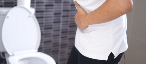 Person holding stomach in pain in front of toilet