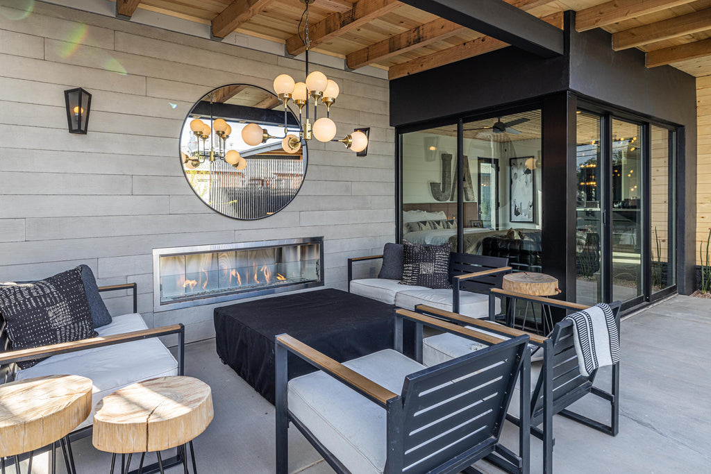 James Judge Outdoor Fireplace surrounded with Wall Theory RealCast Board-form concrete panels, with grey and black outdoor furniture and mirror and light fixture in the centre