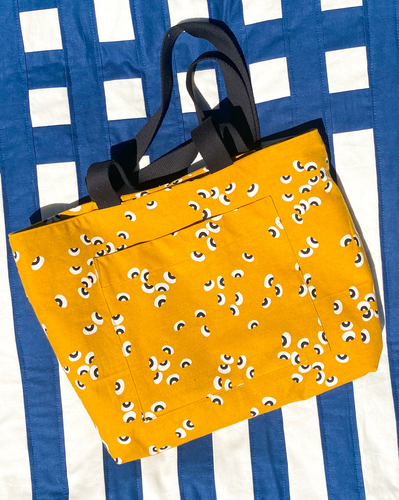 A yellow canvas tote on a blue and white striped quilt. 