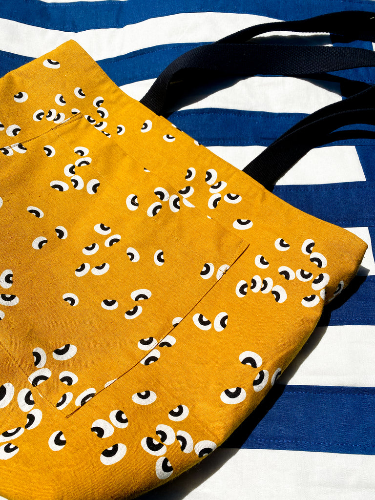 A yellow canvas tote bag with a bean print - close up to show topstitching detail. 