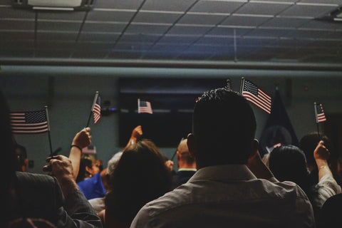 Image of soon to be U.S. Citizens sitting, holding their U.S. Flags during their Naturalization ceremony