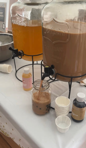 Glass dispensers filled with milk tea and mango green tea. Dispensing milk tea into a cup filled with tapioca