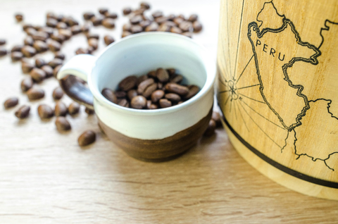 A map of Peru on a container next to an overflowing cup of coffee beans.