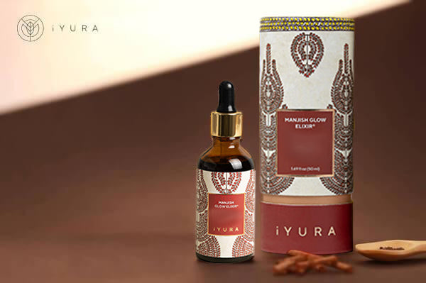 a beautiful photo of Manjish Glow Elixir - iYURA's bestselling night oil - accompanied by its beautifully illustrated, protective cylinder packaging