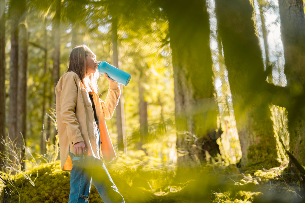 woman in forest with dyln blue bottle woman drinking alkaline water