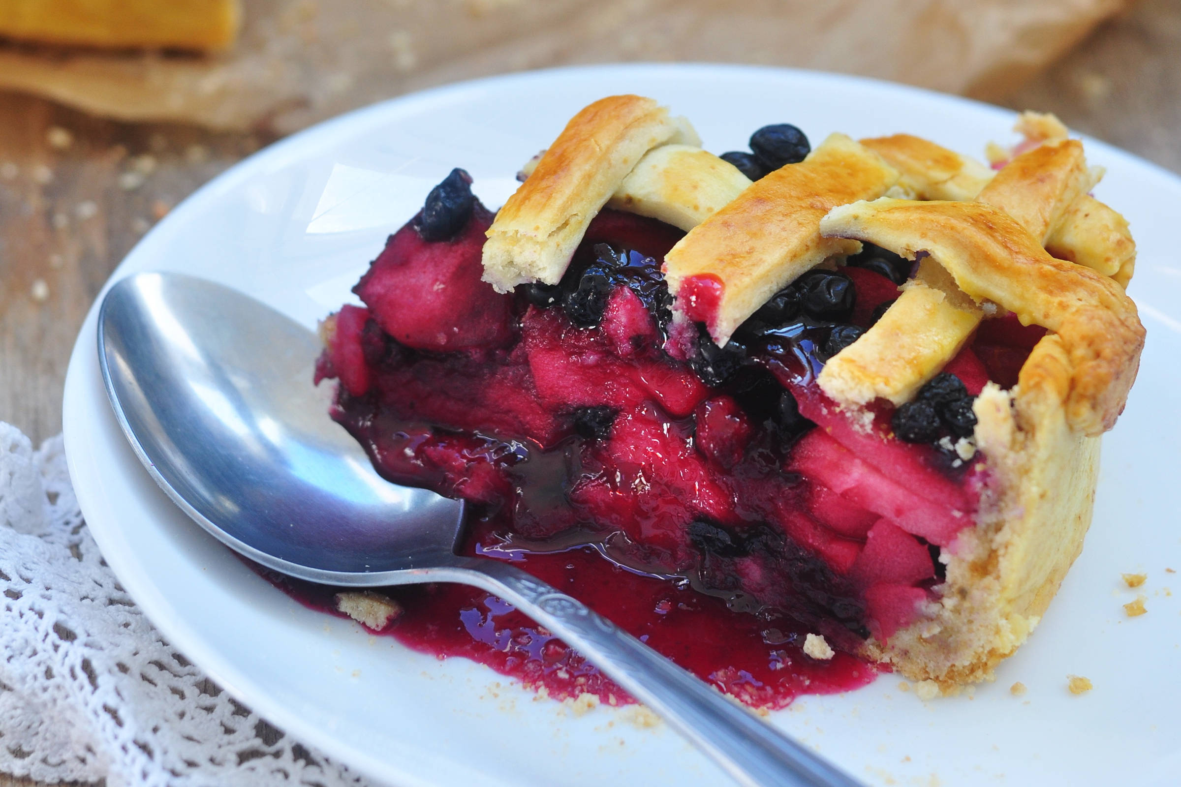 Slice of apple and blueberry pie on a plate with a spoon.