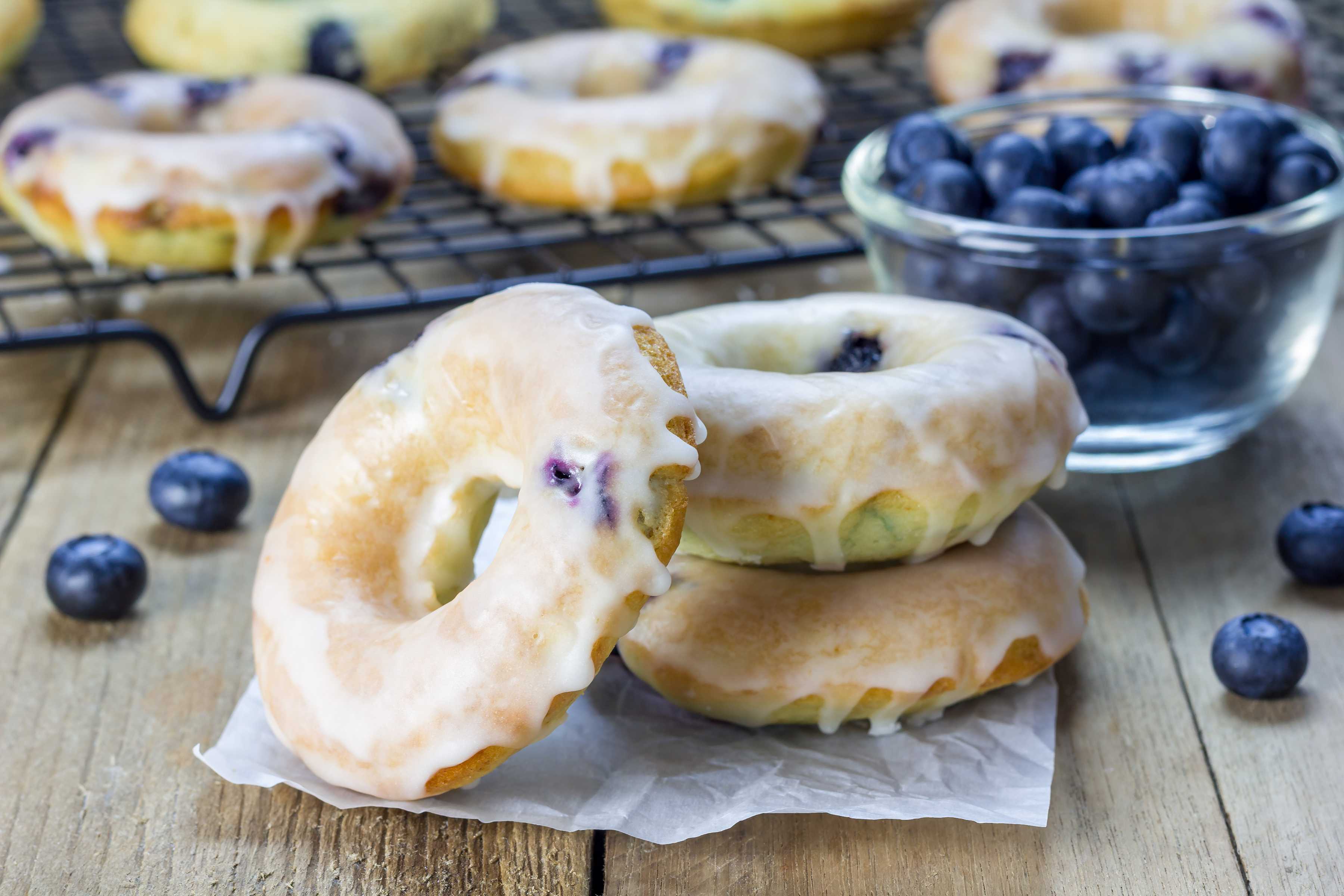 Stack of three baked blueberry donuts with glaze, with more donuts on cooling rack in the background.