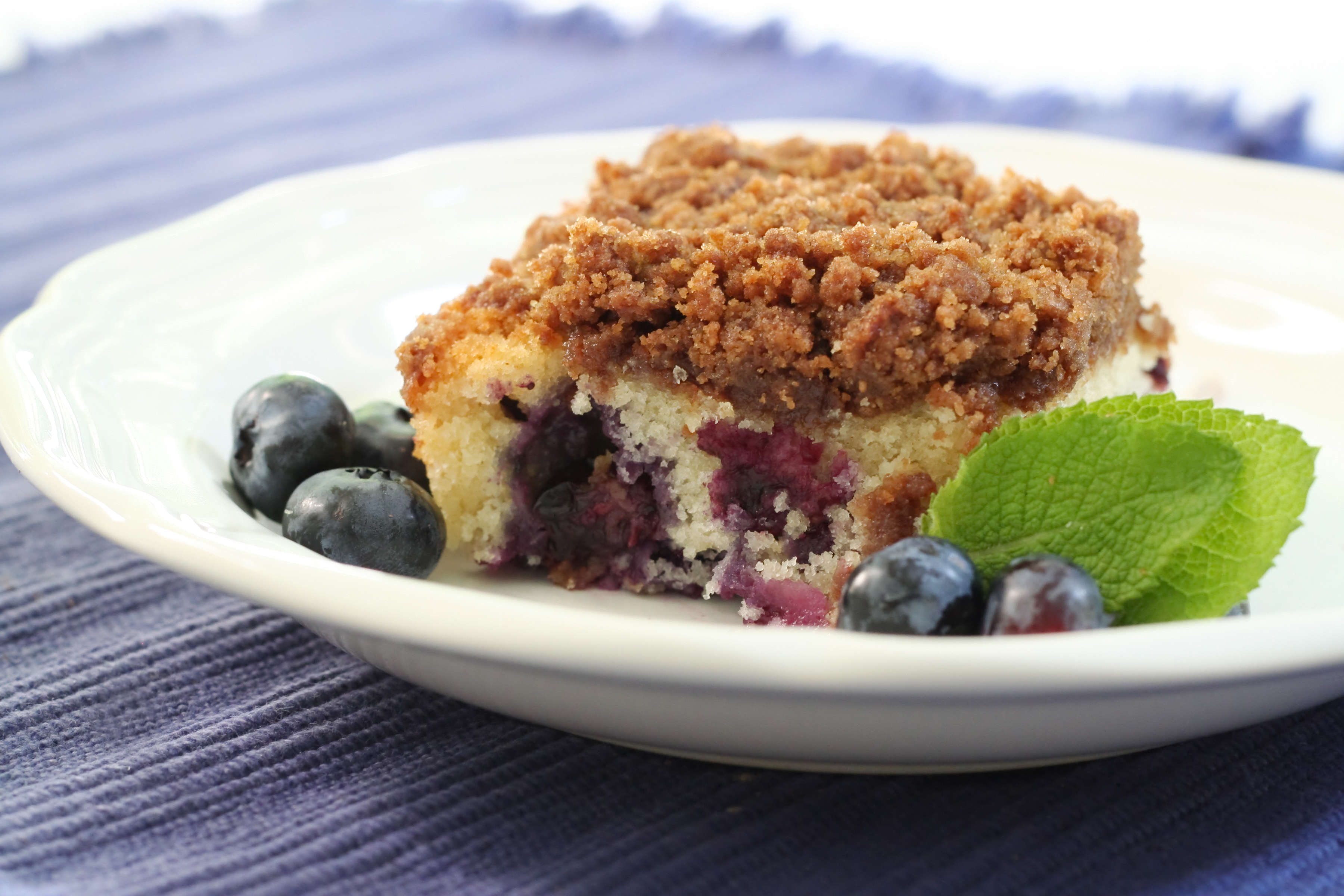 Serving of blueberry buckle cake in a bowl served with fresh blueberries.