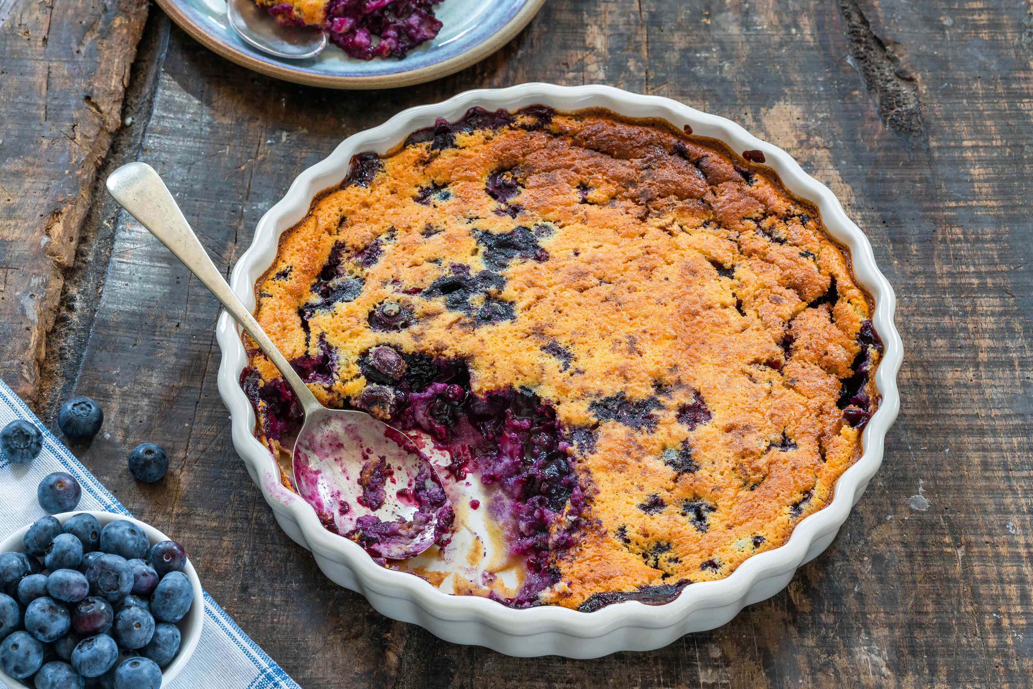 Blueberry clafoutis in baking dish with serving spoon.