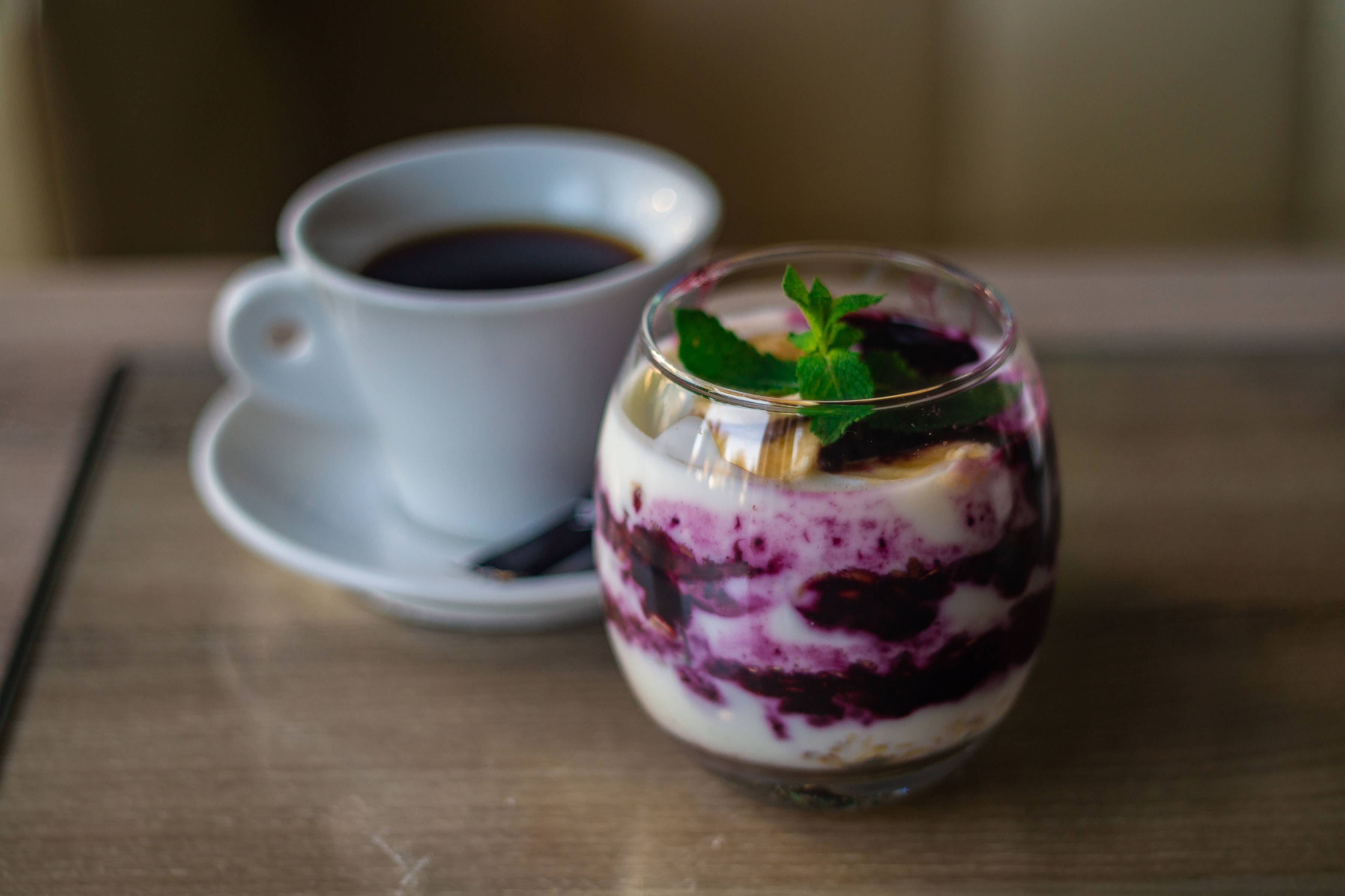 Blueberry overnight oats presented in a glass with a cup of black coffee in the background.