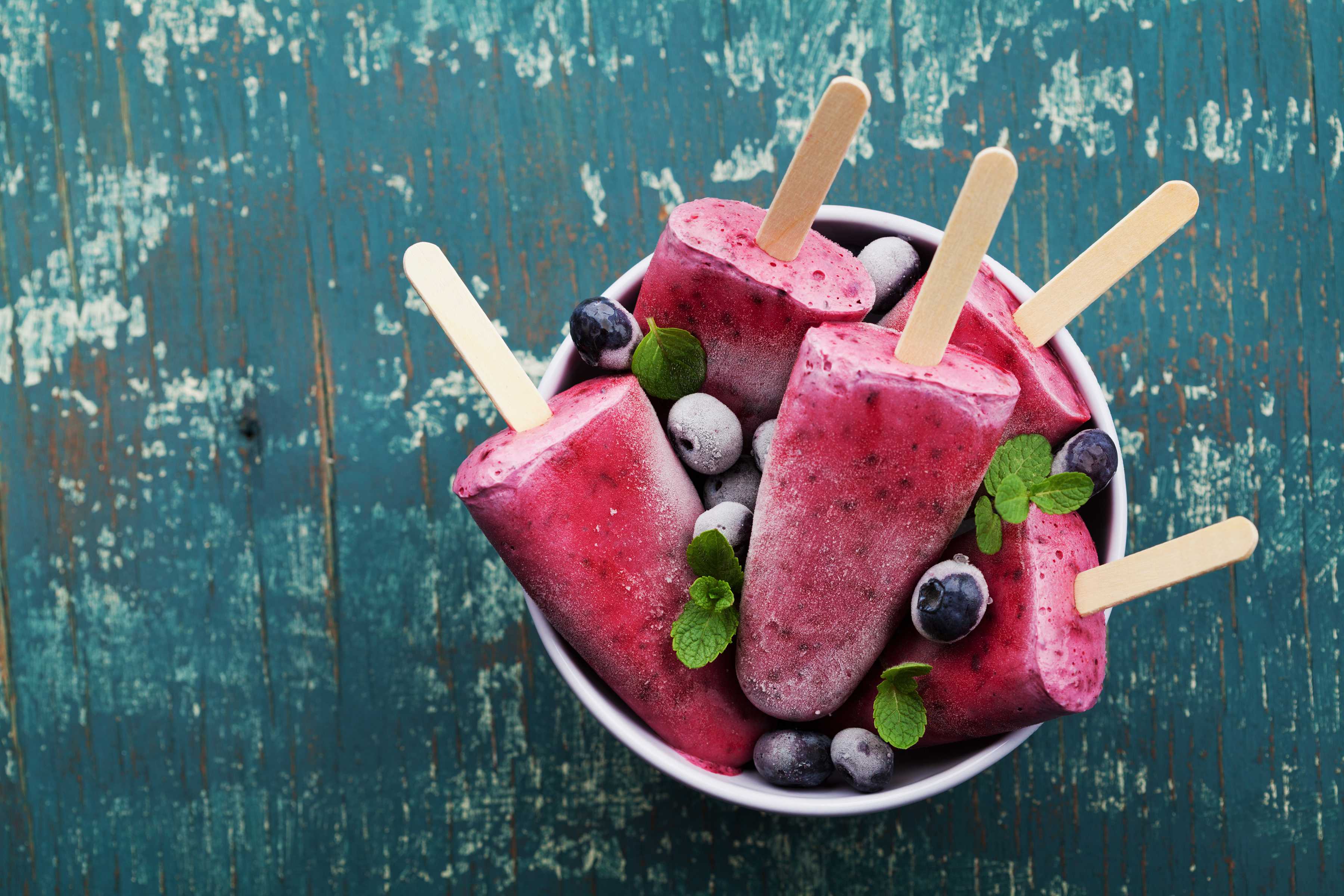 Blueberry popsicles in a bowl with frozen blueberries.