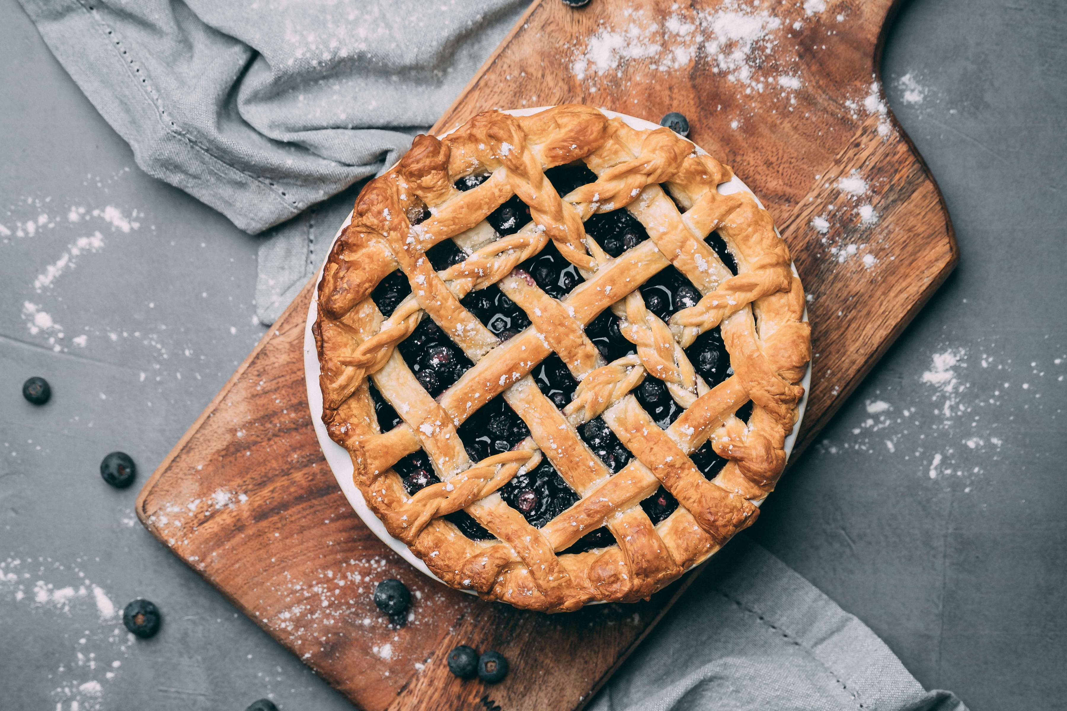 Classic blueberry pie with lattice top on wooden serving board. 