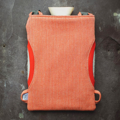 This is a product image of a hot water bottle. It is orange in color with red wavy stripes all over it. The water bottle has straps on either side. The background is granite.