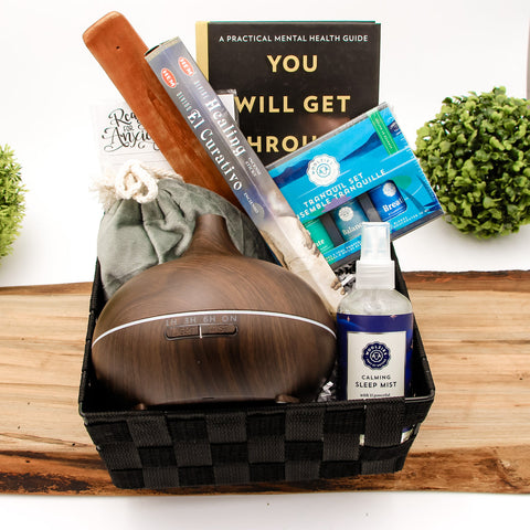 This is a product image of a gift basket. The gift basket consists of a diffuser , a sleeping mist, book and incense. The gift basket is placed on a wooden counter.
