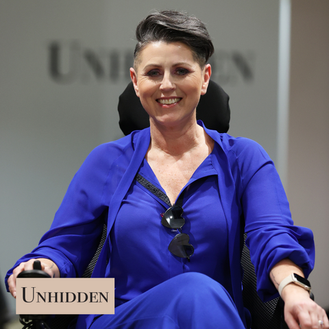 Sandie is a white woman wearing …….. in a power chair on the runway at London Fashion Week. She is smiling at the camera.