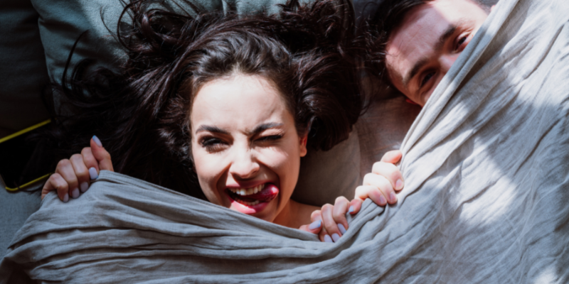 Couple lying in bed smiling under the duvet