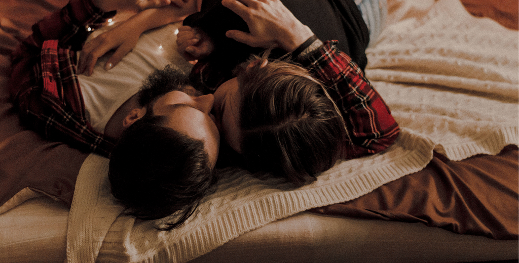 Couple laid on an unmade bed cuddling