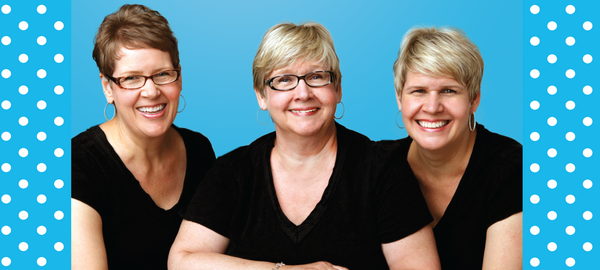 image of three blonde, smiling Duggan Sisters in black t-shirts on a vivid blue backdrop