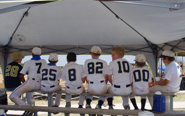 backs of little boys in baseball uniforms siting on a bench