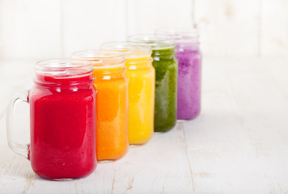 Colored smoothies in mason jars against white background