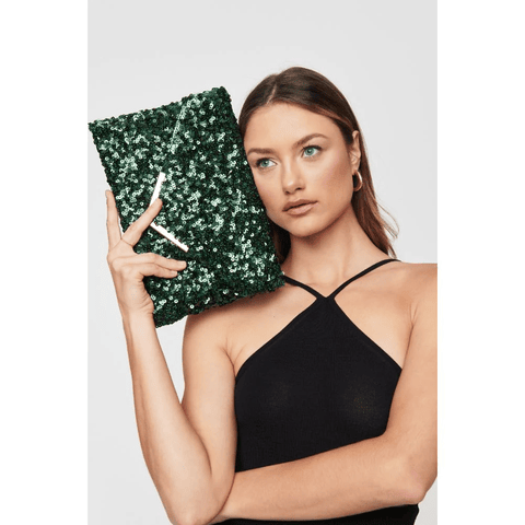 Woman in black evening dress, holds a large, sequinned, green purse to her temple