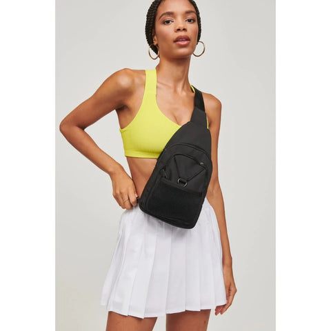 Woman wearing sport crop top and tennis skirt with black sling bag across her chest.