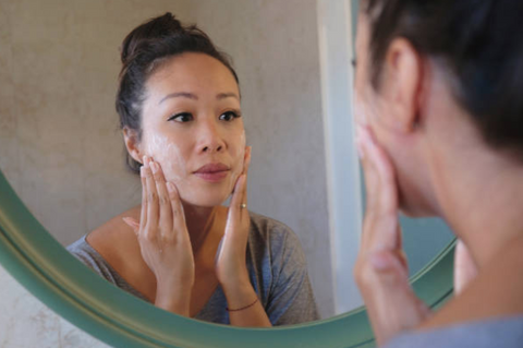 An Asian lady applying skin care products on her skin while looking into the mirror - best skincare products Malaysia - BeautyFoo Mall