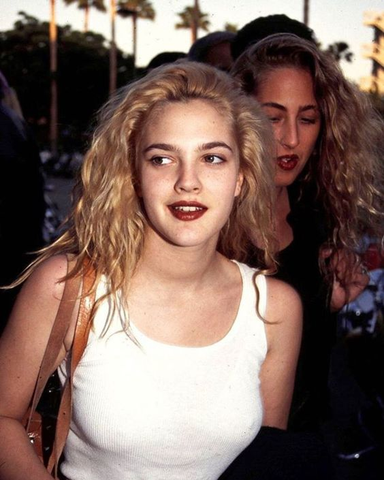 Drew Barrymore embraces grunge-inspired beauty, pairing smudged eyeliner and bold lips with carefree charm