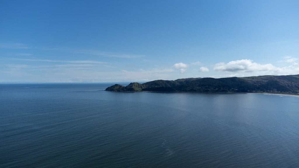 A high drone shot of the coast appearing to stretch out into the ocean on a beautiful day in Mahia