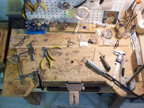 a photo of Vicki's bench with goldsmithing tools scattered about like hammers, pliers, files and foredom.