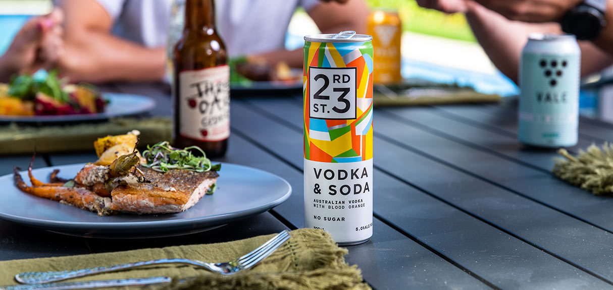 23rd street distillery vodka and soda can on outdoor table with plates of food