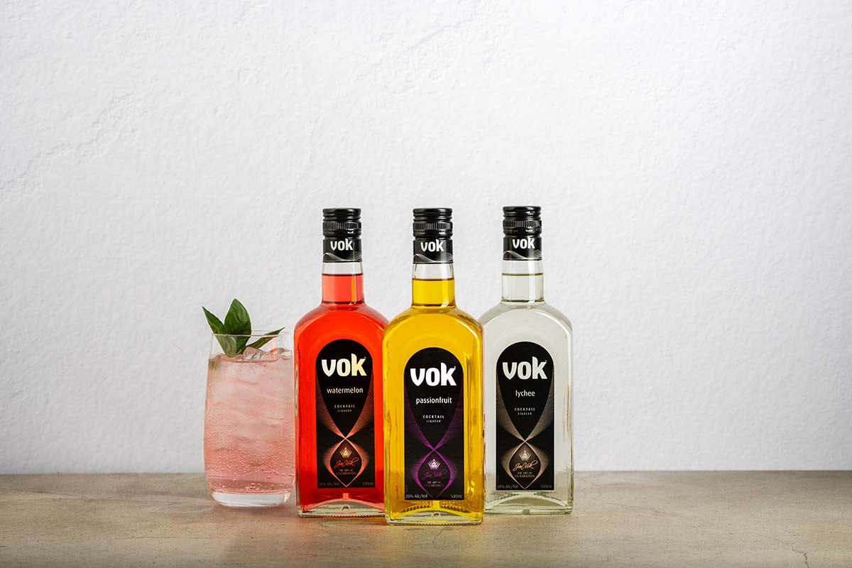three bottles of vok liqueurs on table with pink cocktail in a glass