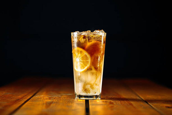 Long Island iced tea in a tall glass in front of a dark black background