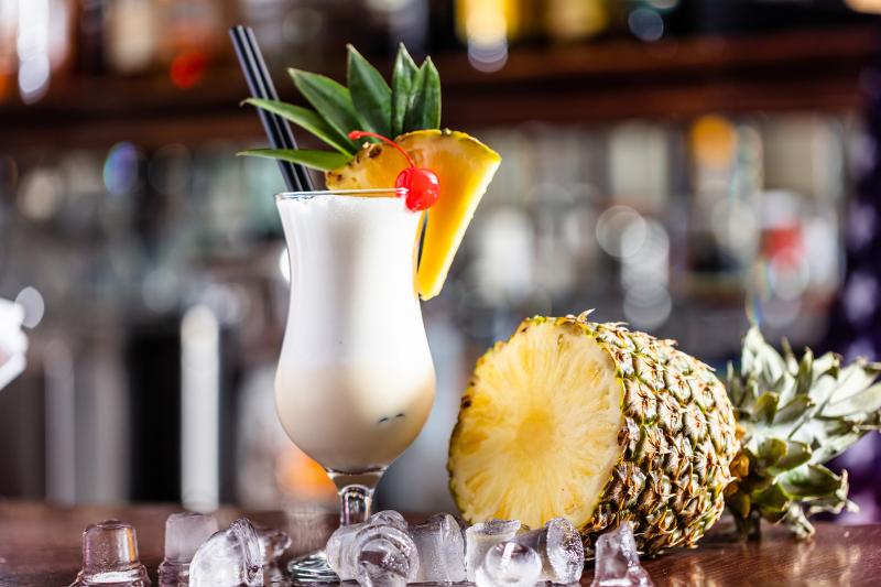 Pina colada cocktail on a bar with a cut pineapple beside it