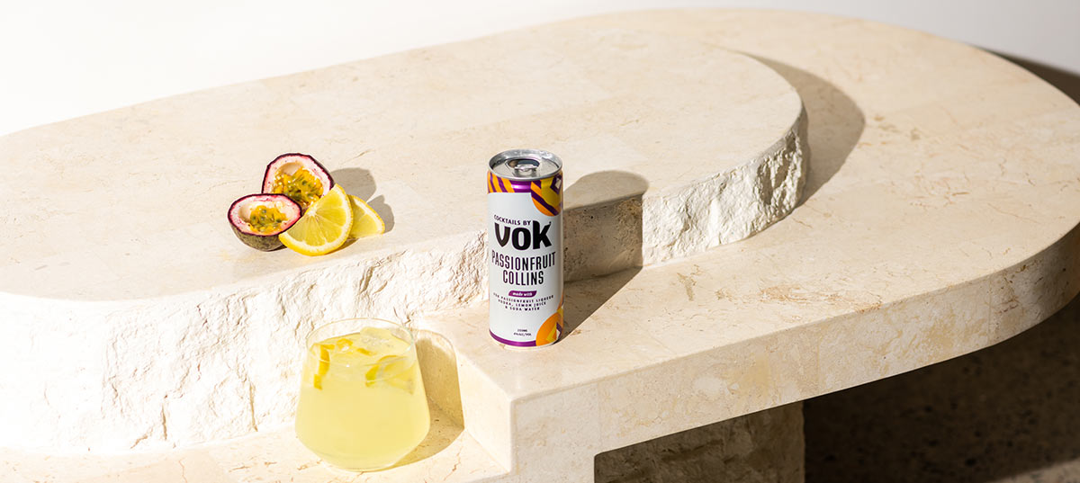 can of Vok passionfruit collins on a table with some cut passionfruit