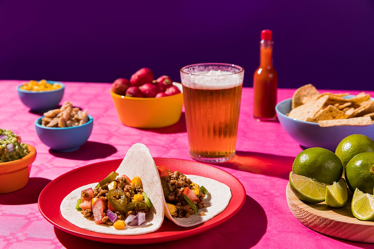 mexican food and a beer in a glass on a pink table