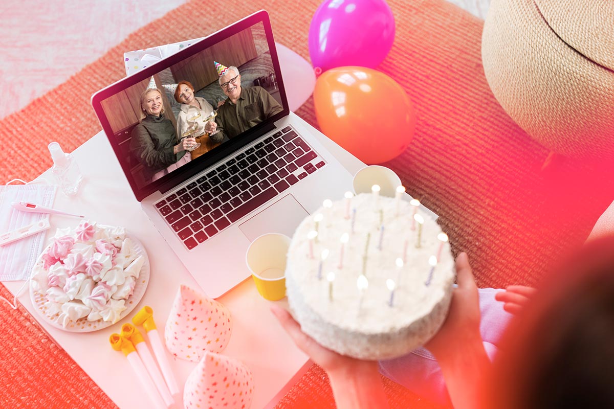 a person holding a birthday cake in front of a laptop celebrating virtually with family members