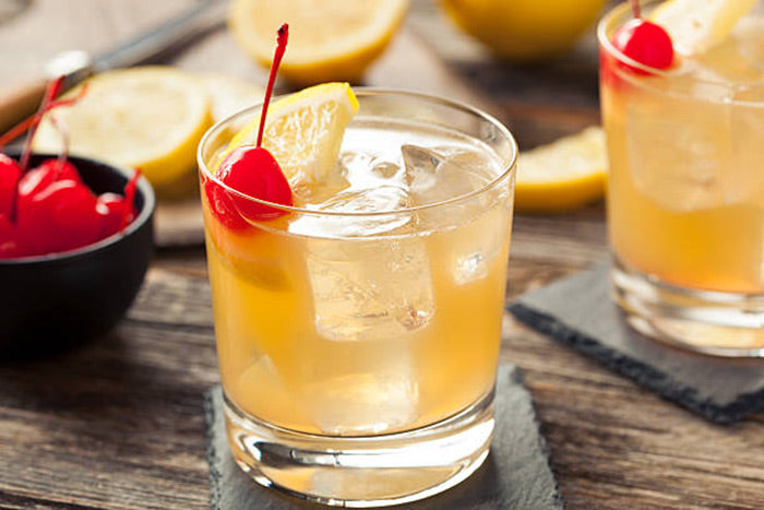 Whiskey Sour cocktail with lemon wedge and a cherry