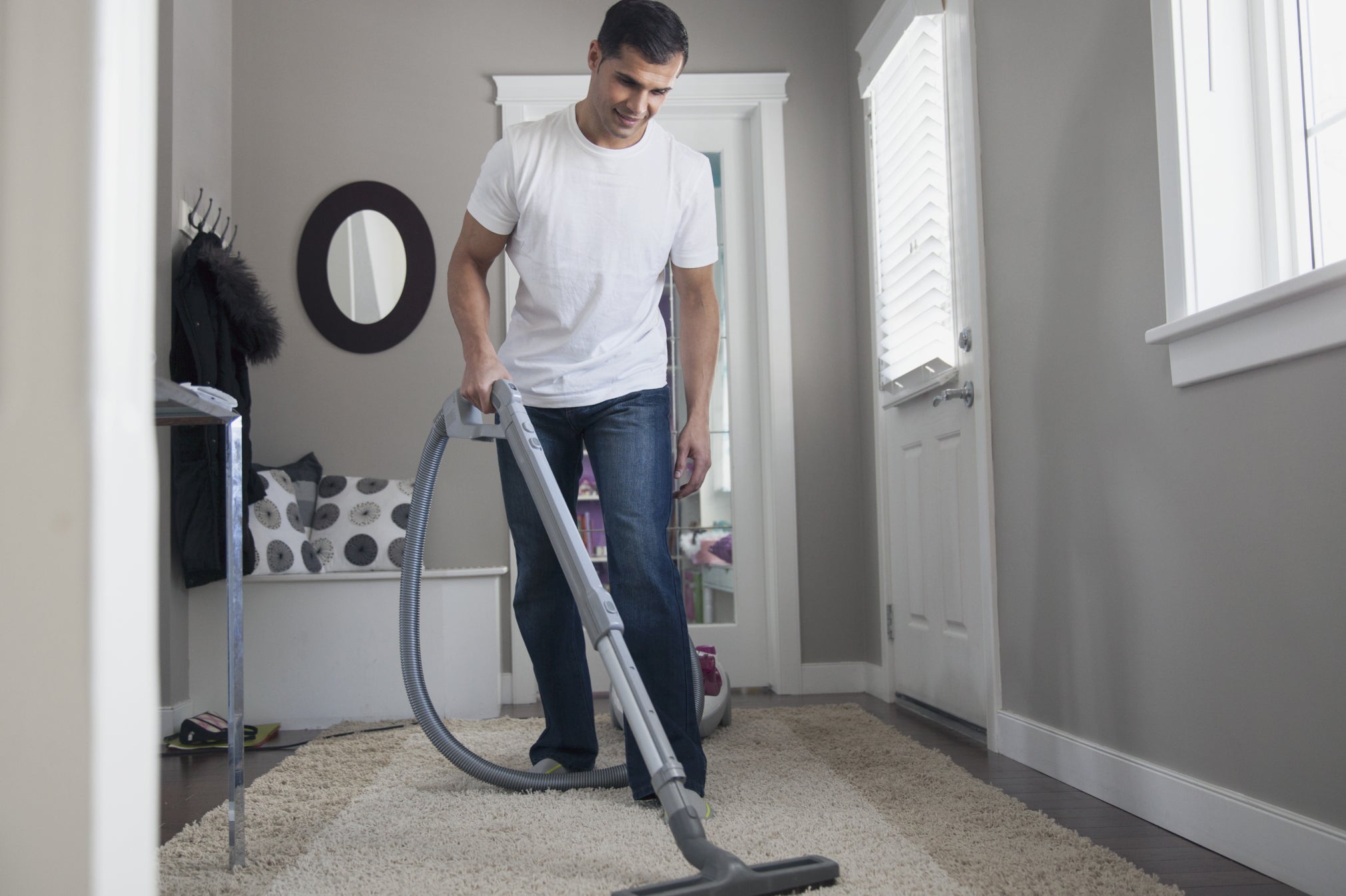 Man wearing t-shirt and jeans hovering rug in living room