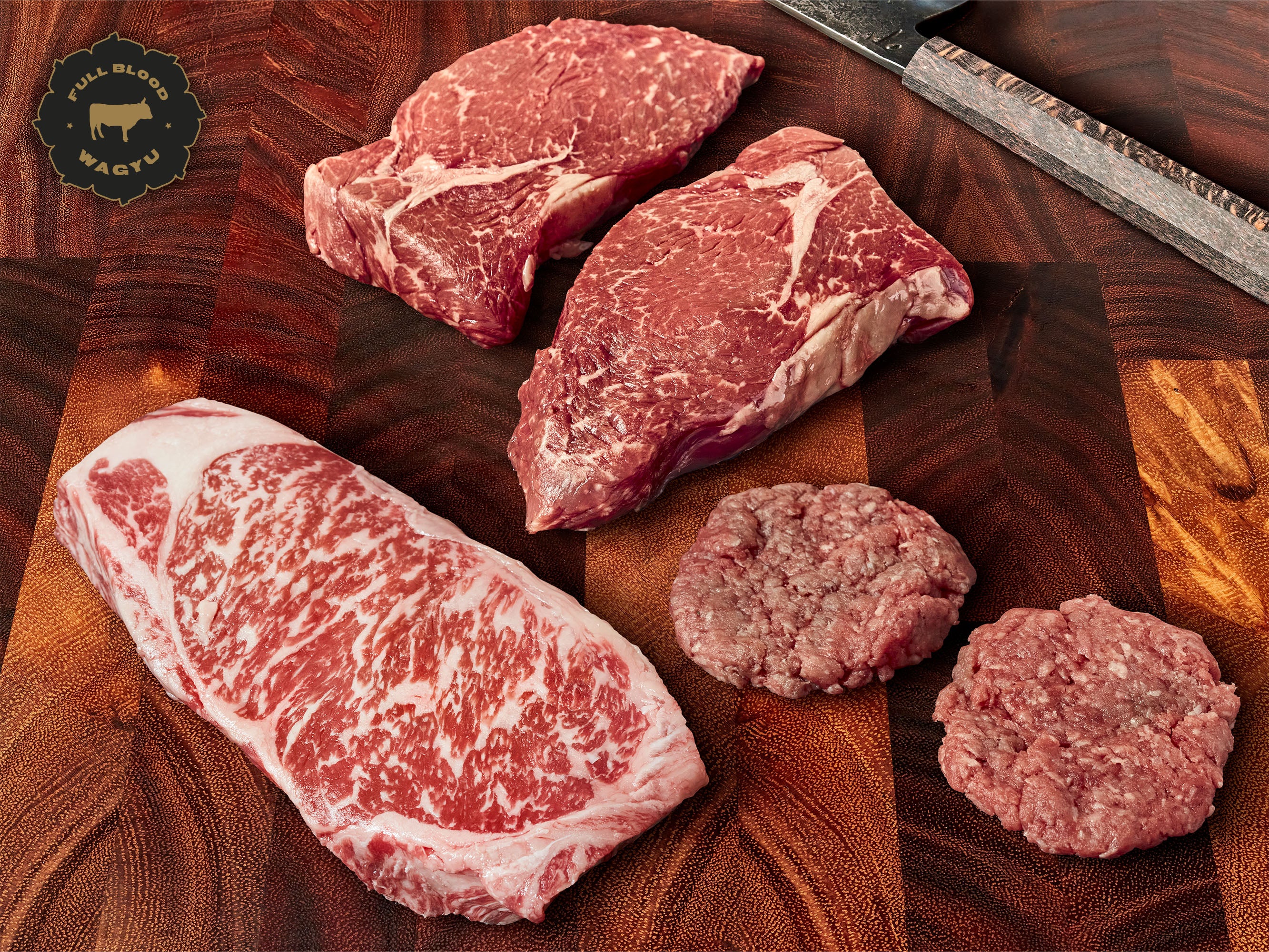 Assorted raw Wagyu beef cuts on a wood-patterned surface with a knife and cutting board.