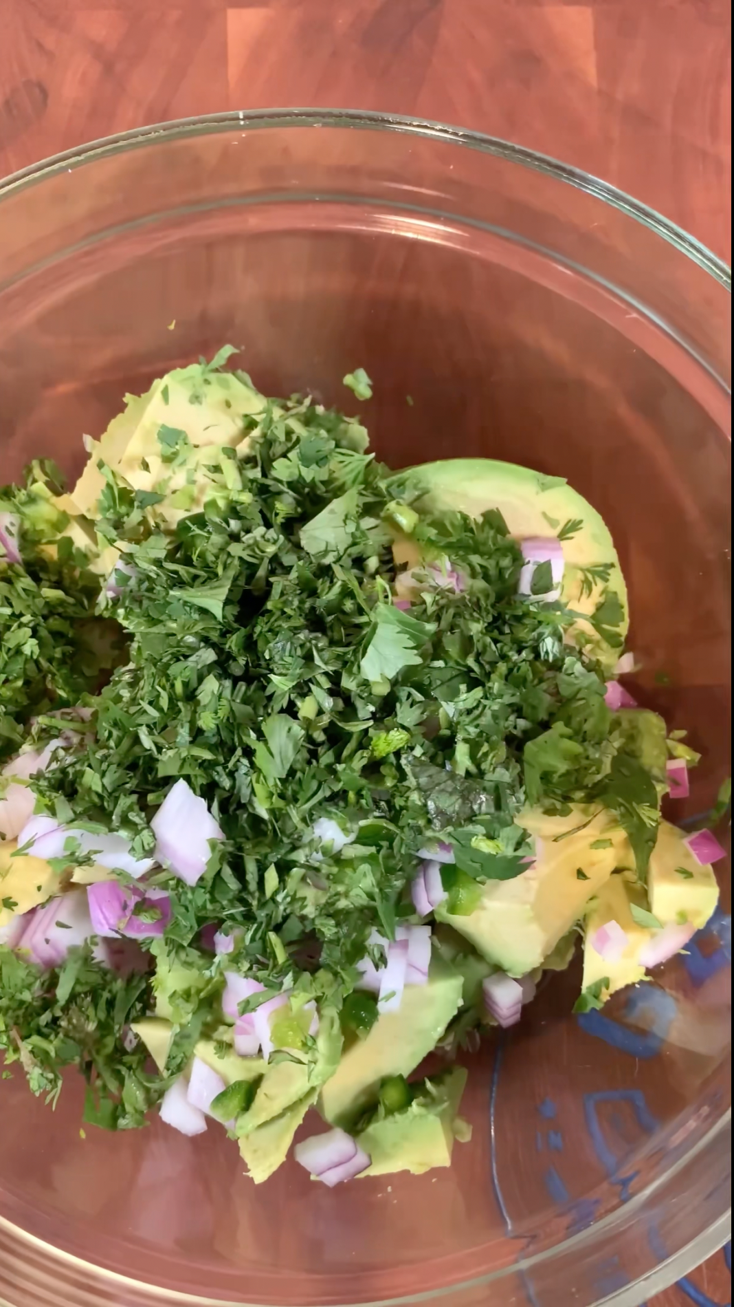 Ingredients for homemade guacamole in a glass bowl. Avocado, lime, cilantro, red onion, jalapeños, and kosher salt