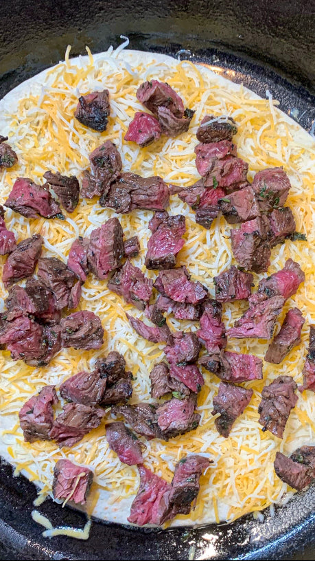 Skirt steak quesadilla with cheese being assembled in a cast iron pan. 