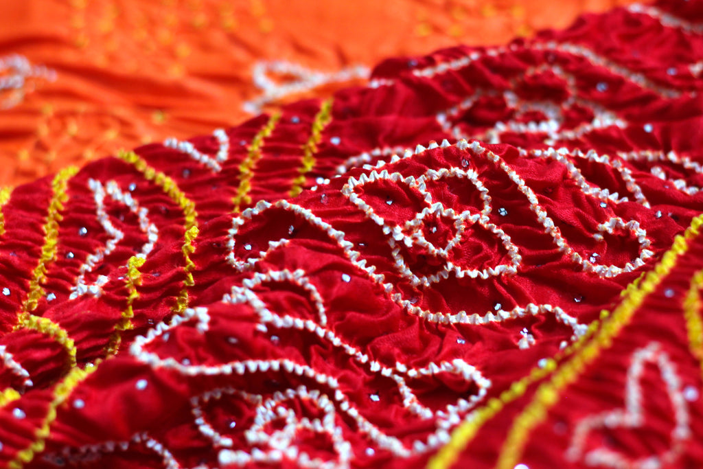 Close up of Chakor's Mesmerising Bandhani saree in orange and red colour adorned with delicate & sparkling Mukaish embroidery.