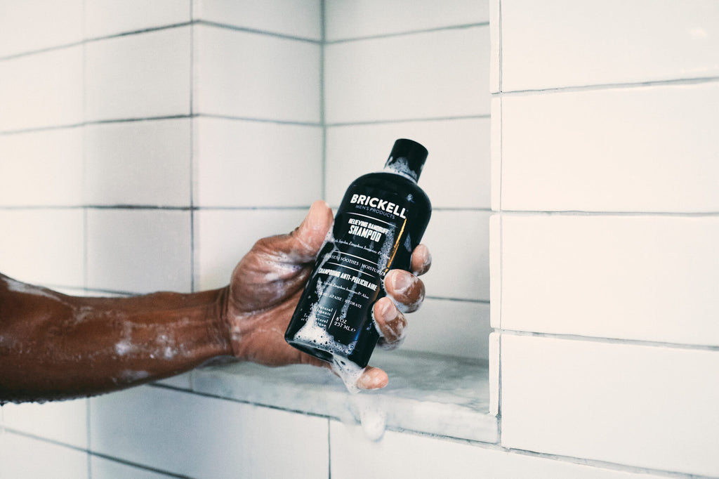 Čovjekova ruka pod tušem poseže za bocom šampona.